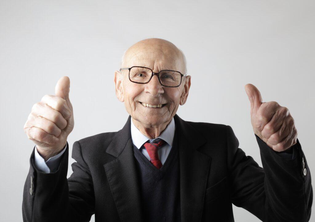 Older man in business suit smiling with both thumbs up.